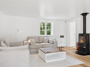Ein modernes Wohnzimmer mit einer Couch, einem Couchtisch, einem Kamin und einem Fenster mit Blick auf Grünflächen.