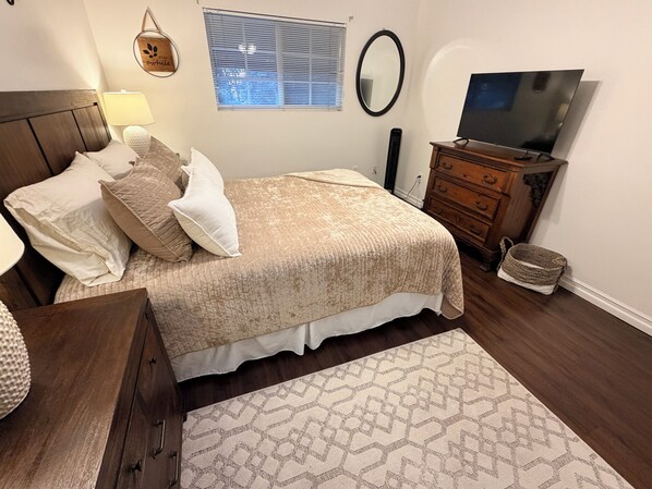 Un dormitorio con cama, cómoda, televisor, ventana y decoración en la pared.