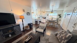 A living room with a TV, sofa, coffee table, and a kitchen in the background.