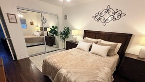 A bedroom with a large bed, a mirror, a wooden headboard, bedside tables, and a potted plant.
