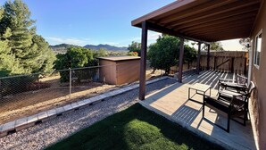 A covered patio with a view of mountains, a fenced yard, and a small shed.