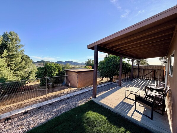 Un patio techado con vistas a las montañas, un jardín cercado y un cobertizo pequeño.