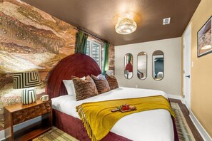 A hotel room with a large bed, a nightstand, a lamp, and a wall with three mirrors.