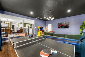 A ping pong table, a sofa, a foosball table, and a poster on a wall.