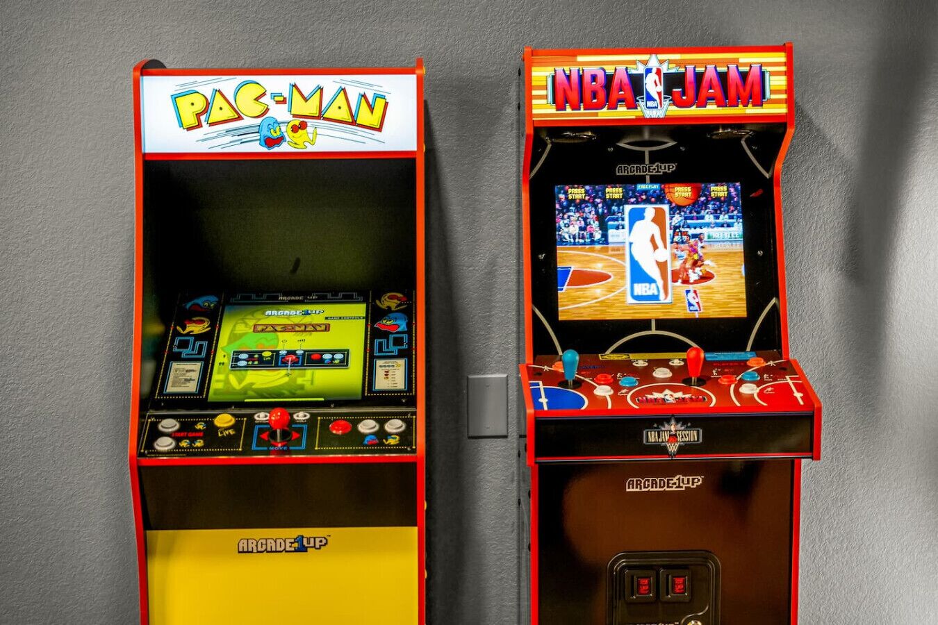 Kaksi peliautomaattia, toisessa lukee ”PAC-MAN” ja toisessa ”NBA JAM”. Molemmissa on selvästi näkyvissä ohjauspaneelit ja näytöt.