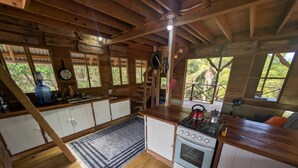 Eine rustikale Küche mit Holzschränken, einem Herd und einem großen Fenster mit Blick auf Grünfläche.
