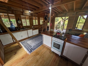 Eine rustikale Küche mit Holzschränken, einem Herd und einem großen Fenster mit Blick auf Grünfläche.