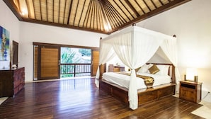 A spacious room with a wooden floor, a four-poster bed with white bedding, a nightstand with a lamp, and a view of greenery through a sliding door. - Huge Private Pool Villa Atala Canggu Seminyak 4BR (Kerobokan)