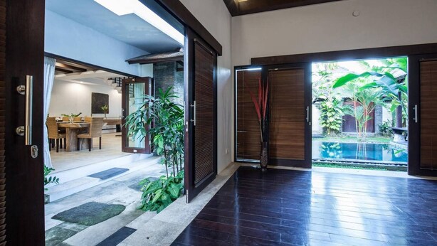 A modern interior with a dining area, a pool, and a view of lush greenery. - Huge Private Pool Villa Atala Canggu Seminyak 4BR (Kerobokan)