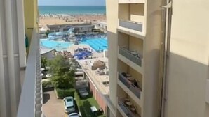 Een hoog gebouw met meerdere balkons met uitzicht op een strand en een zwembad.