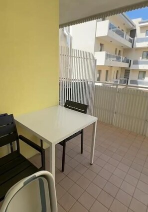 Ein Balkon mit weißem Tisch und Stühlen, einer gelben Wand und Blick auf angrenzende Gebäude.