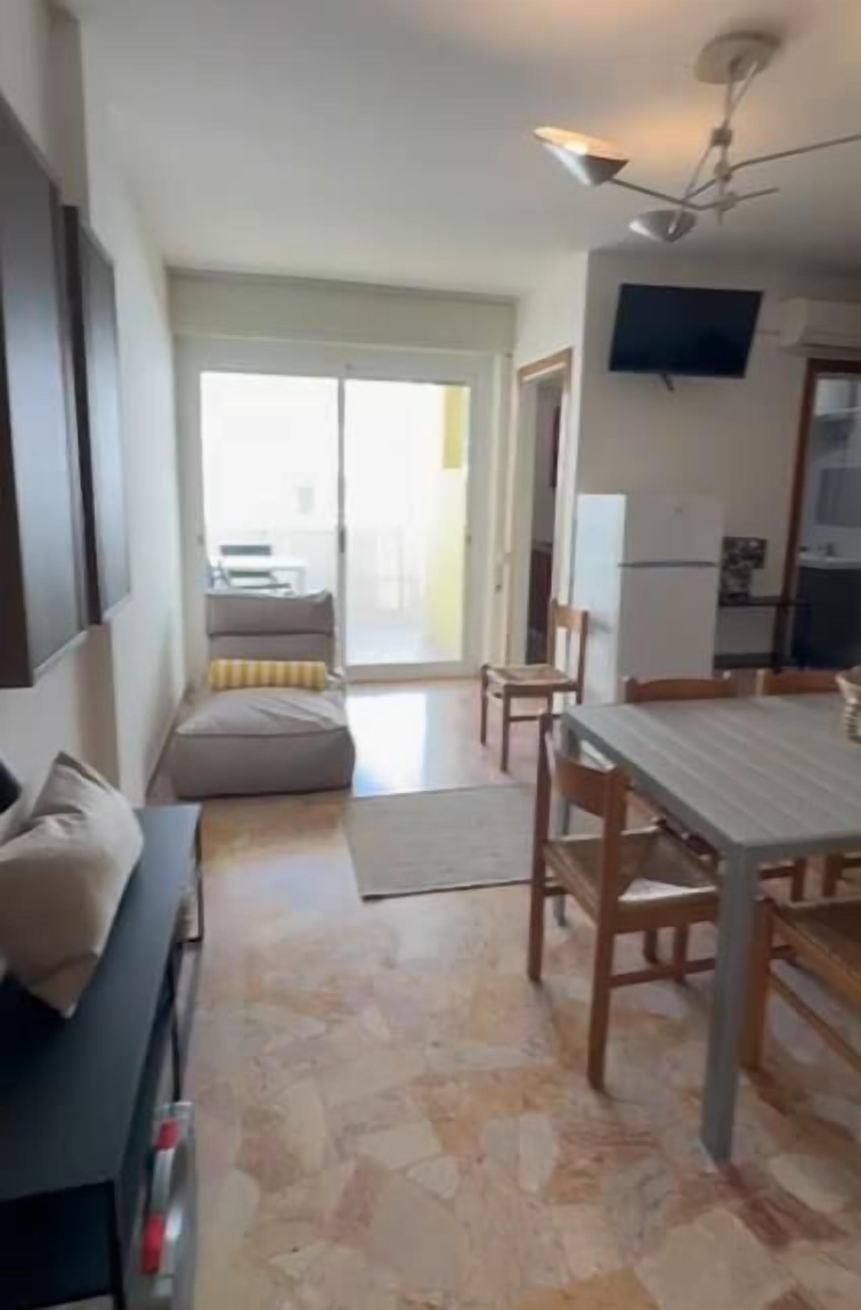 Ein Wohnzimmer mit Sofa, einem Esstisch mit Stühlen, einem an der Wand befestigten Fernseher und einem Deckenventilator.