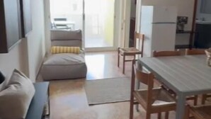 Een woonkamer met een bank, een eettafel met stoelen, een aan de muur bevestigde televisie en een plafondventilator.
