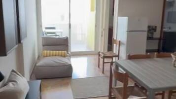 Ein Wohnzimmer mit Sofa, einem Esstisch mit Stühlen, einem an der Wand befestigten Fernseher und einem Deckenventilator.