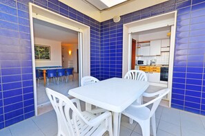 Ein Essbereich mit weißem Tisch und Stühlen, blauen Fliesenwänden und einer durchgehenden Tür erkennbaren Küche.
