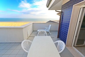 A balcony with a white table and chairs, a view of the beach, and a blue tiled wall. - Lignano Top-floor Flat Near Center (Lignano Sabbiadoro)