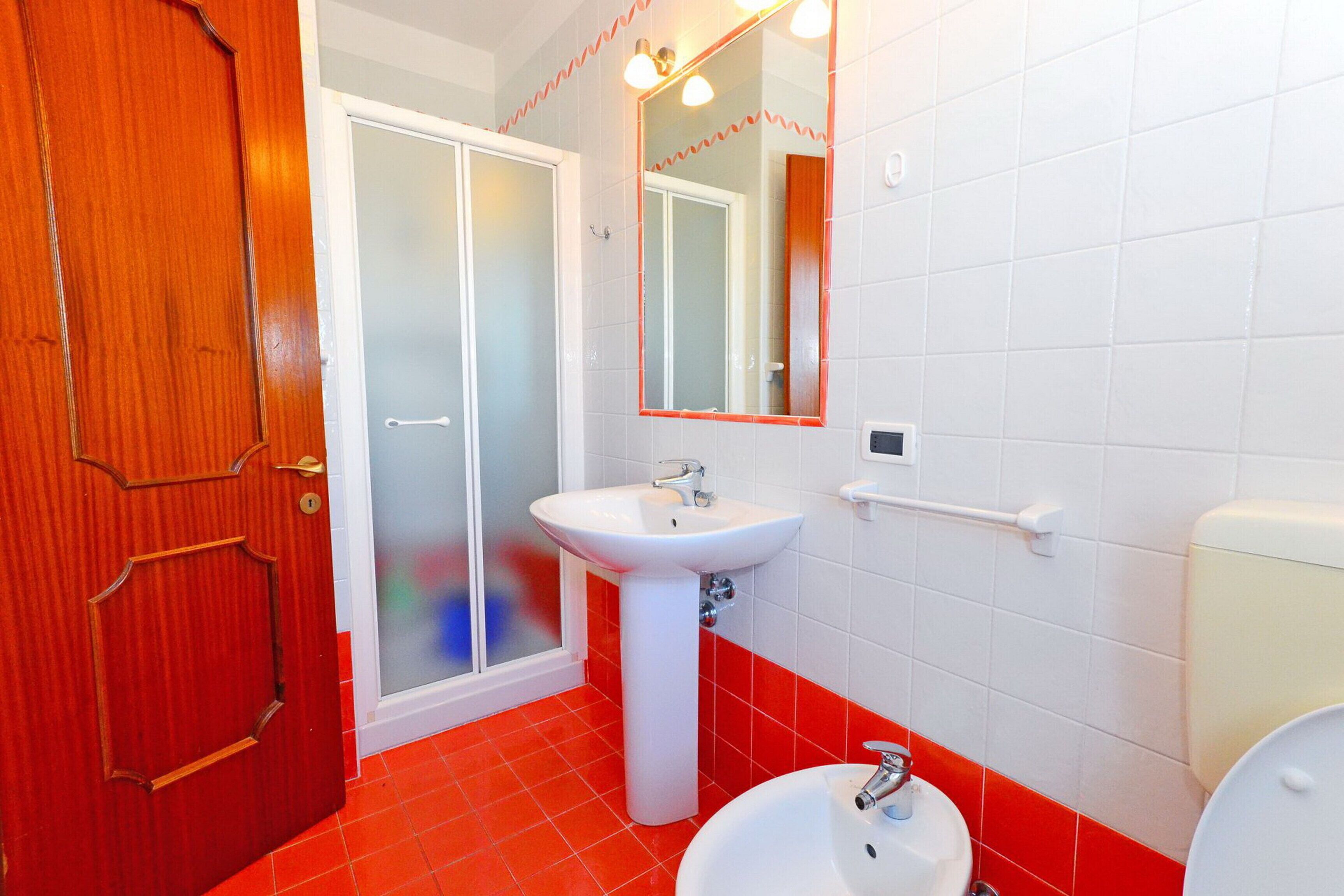 A bathroom with a wooden door, a white sink, a mirror, and a toilet.