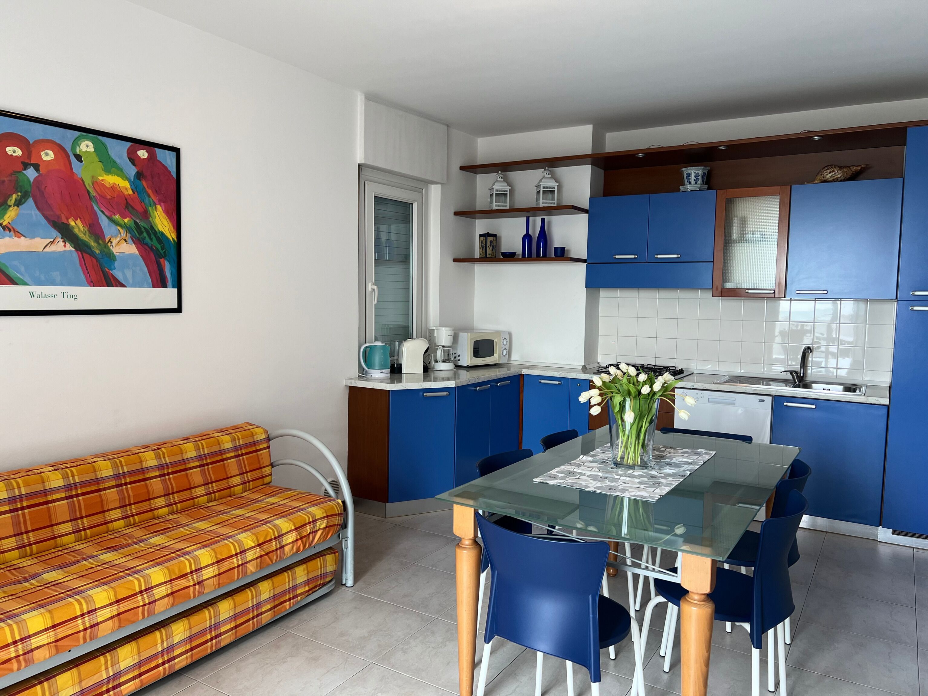 Une cuisine moderne avec des meubles de rangement bleus, une table à manger en verre et un canapé coloré.