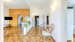 A spacious hallway with a patterned floor, a reception desk, wicker chairs, and a flat-screen TV.