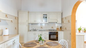 A kitchen with white cabinets, a round wooden table with placemats, a white chair, and a potted plant.