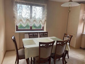 A dining area with a table, chairs, a window with curtains, and a cabinet. - Namas Nida (Dreverna)
