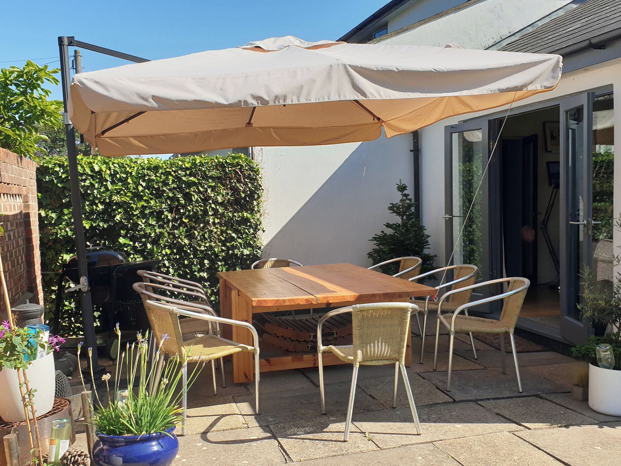Une terrasse extérieure avec une table en bois et des chaises en osier, un barbecue et un grand parasol.
