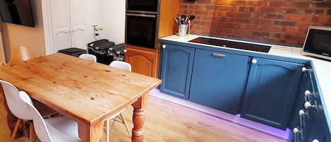 A kitchen with wooden cabinets, a dining table, chairs, a TV, a stove, and a brick wall.