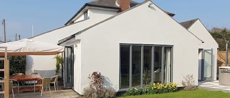 A modern house with a white exterior, a large sliding glass door, and a small garden with yellow flowers.