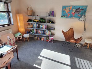 Um quarto de brincar infantil com estante, brinquedos, mapa e piano.