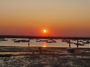 A sunset over a calm body of water with boats and a person standing on the shore. - Island Retreat (Colchester)