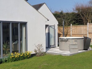 Ein modernes Haus mit großen Glasfenstern, einem Whirlpool und einem Garten voller gelber Blumen.