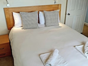 A neatly made bed with a wooden headboard, two patterned pillows, and rolled towels on the bed. - Island Retreat (Colchester)