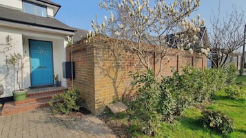 A residential house with a blue door, brick wall, and a garden with various plants.