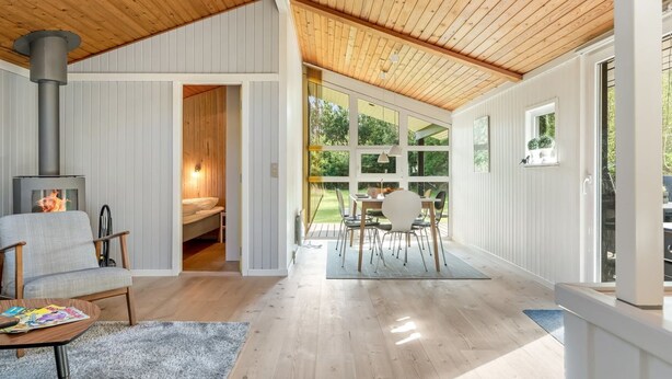 Interior moderno com teto de madeira, lareira, área de jantar com mesa e cadeiras, e vista para o exterior.