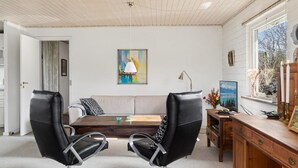 A modern living room with a wooden ceiling, a large painting, a wooden desk, and two black leather chairs.