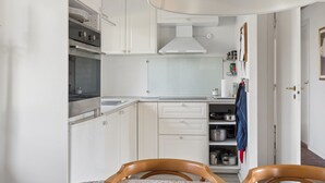A kitchen with white cabinets, a stove, and a dining area with two wooden chairs.
