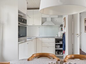 Una cocina con armarios blancos, una estufa y una zona de comedor con dos sillas de madera.