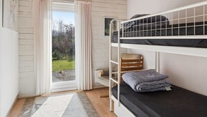 A bunk bed room with a view of a garden through a window, a wooden ceiling, and a hanging light fixture.
