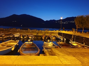 Un port de plaisance au crépuscule, avec des bateaux amarrés, un lampadaire et des montagnes en arrière-plan.