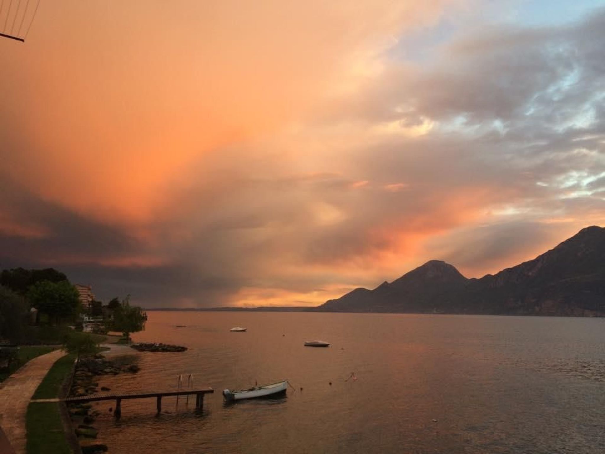 Um lago tranquilo com barcos, um cais e montanhas ao fundo.