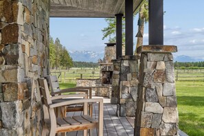 A stone fireplace, wooden chairs, and a view of mountains. - Newly Listed Home on 13 Acres with Firepit and Wood Burning Fireplace (Whitefish)