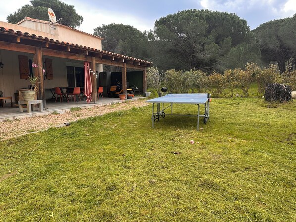 A house with a covered patio, outdoor seating, and a ping pong table in a grassy yard.