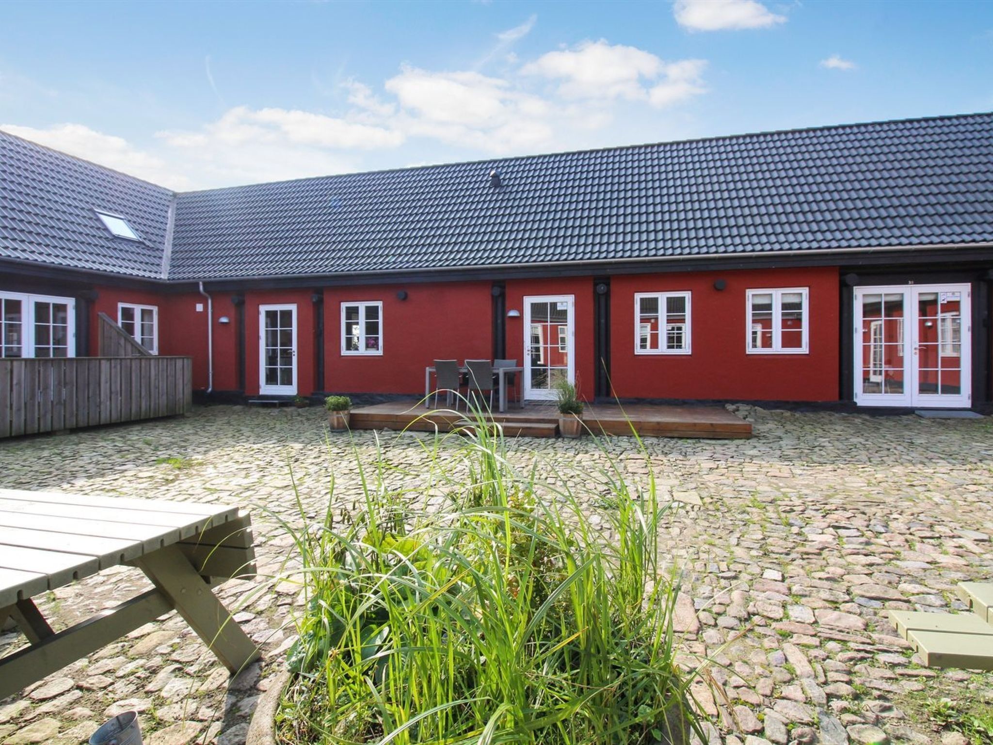 A red building with a tiled roof, a courtyard with cobblestone ground, and a wooden bench.