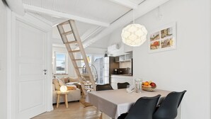 En matplats med ett bord, stolar, en kristallkrona och en stege som leder upp till ett loft.