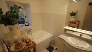 Un baño con bañera, lavabo, espejo y ventana con una planta.