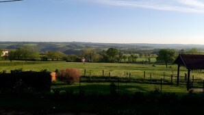 Un paysage rural avec un champ délimité par une clôture, un petit bâtiment et des collines à l’horizon.