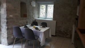 Un comedor con una mesa preparada para cuatro personas, sillas, una ventana con vistas y una pared de piedra.