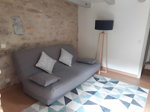 Ein graues Sofa mit gemusterten Kissen, ein geometrischer Teppich und eine stehende Stehlampe in einem Zimmer mit Steinwand und wei ßer Tür.