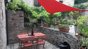 Un patio con una mesa y sillas de piedra, una parrilla y plantas en macetas.