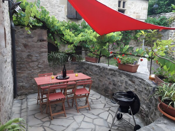Un patio con una mesa y sillas de piedra, una parrilla y plantas en macetas.